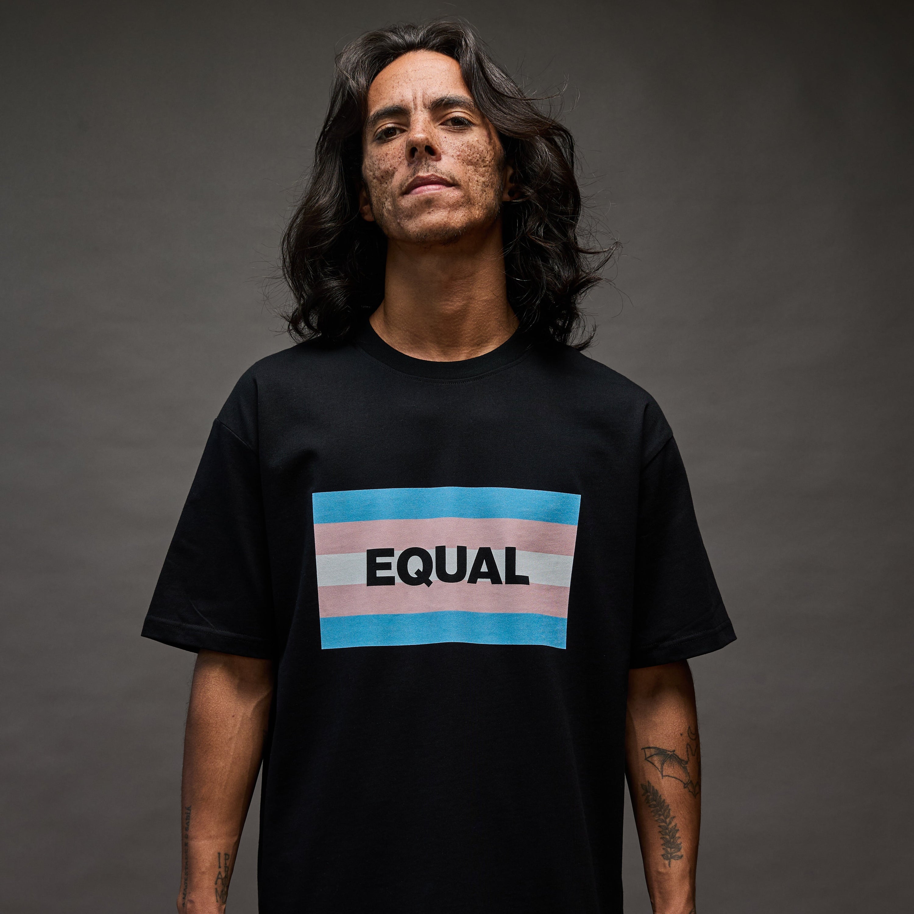Person wearing a black t-shirt with 'EQUAL' and a rainbow stripe design on a dark background