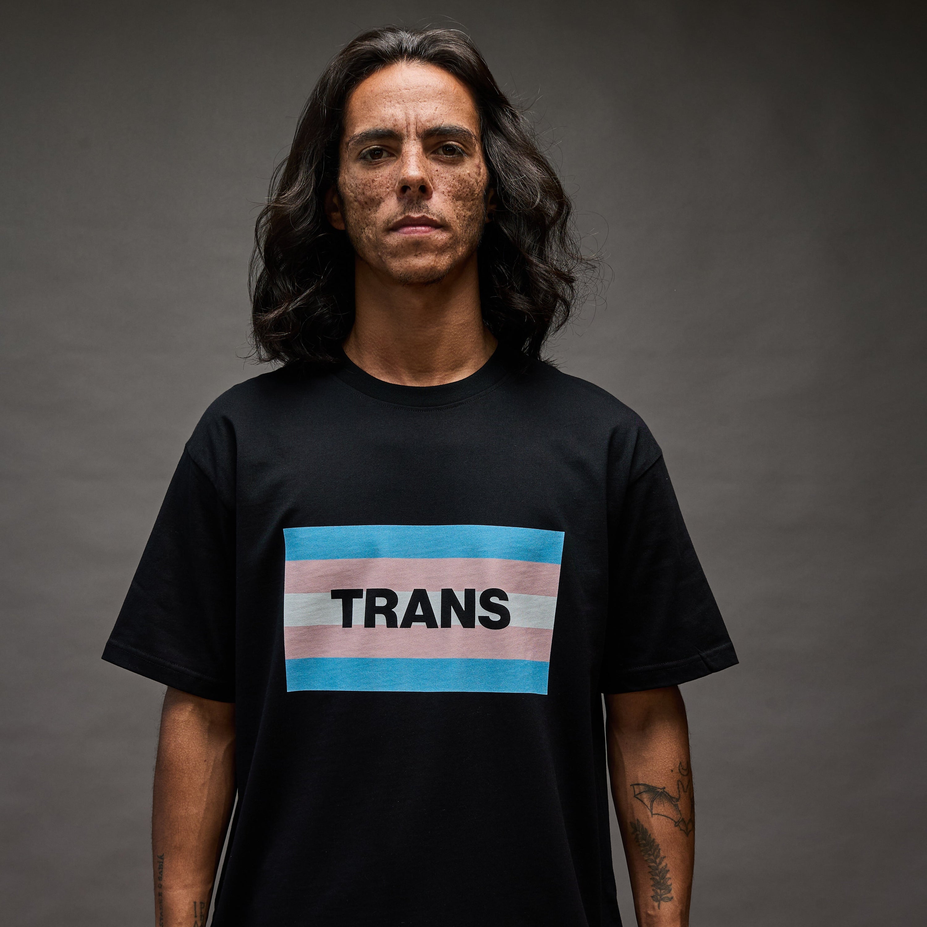 Person wearing a black t-shirt with a transgender flag design and the word 'TRANS'.