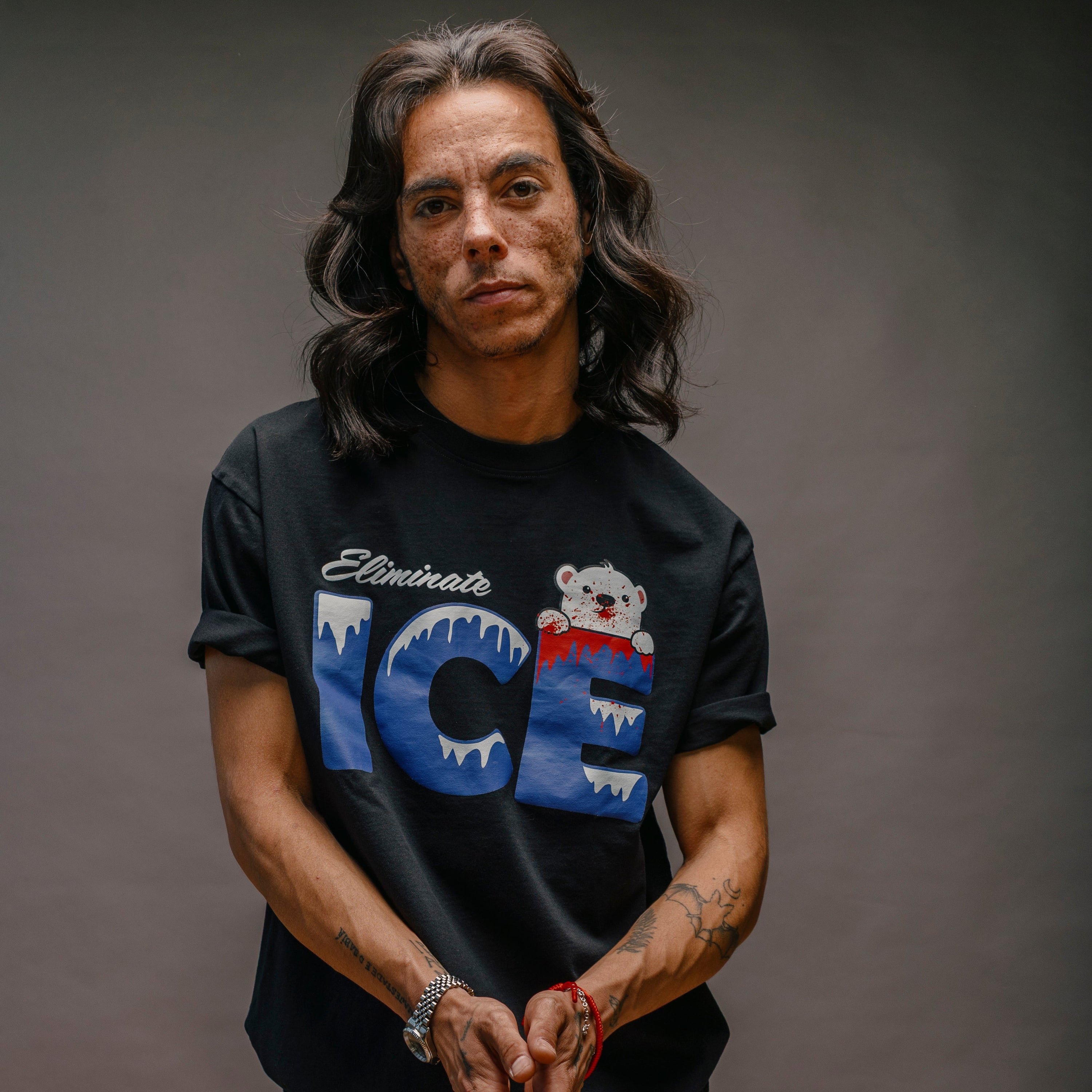 Person wearing a black t-shirt with a graphic design on a gray background. THE T-SHIRT SAYS ELIMINATE ICE.