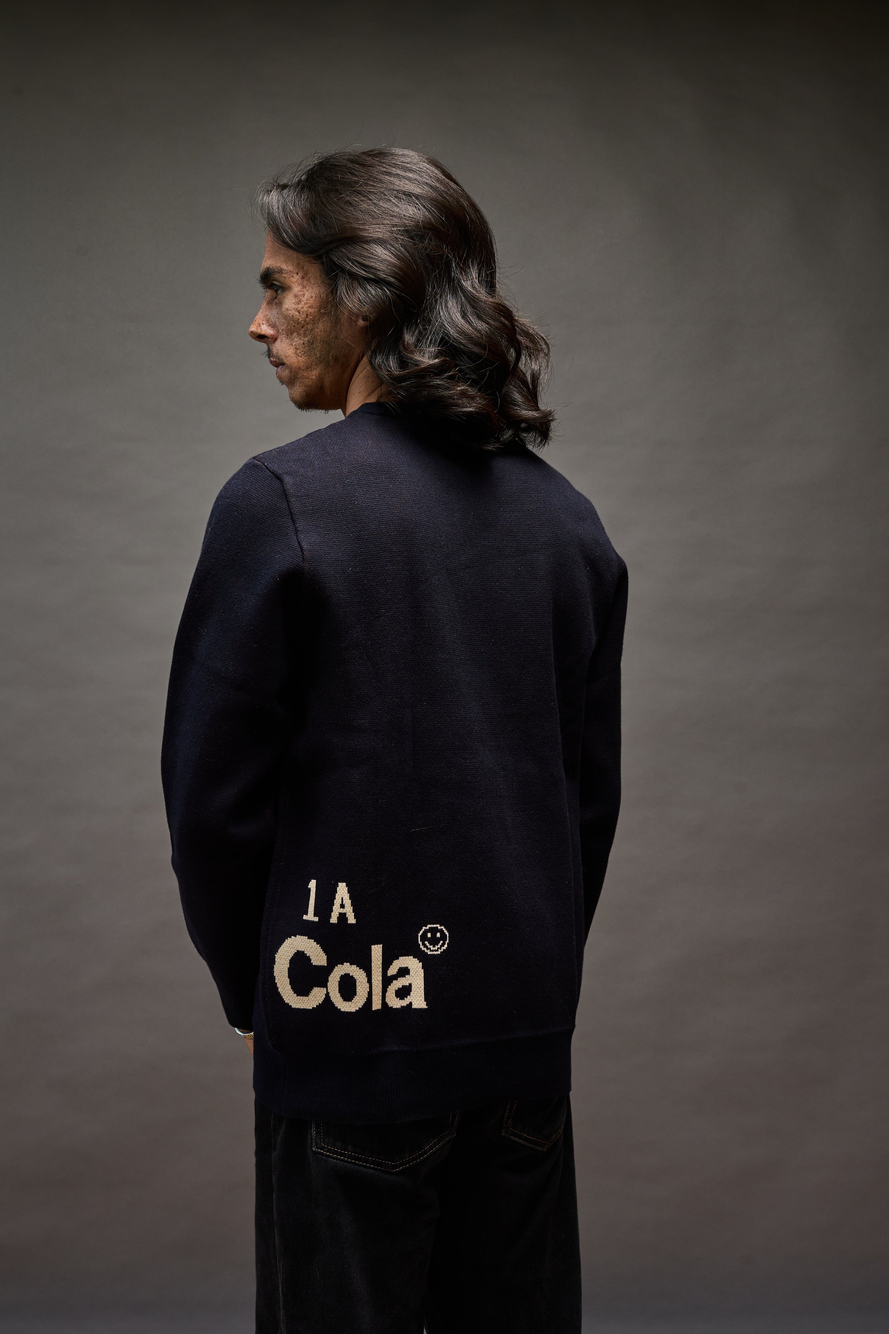 “Back view of Cola Corporation burning flag  navy blue cotton sweater. 1A indicates First Amendment"
