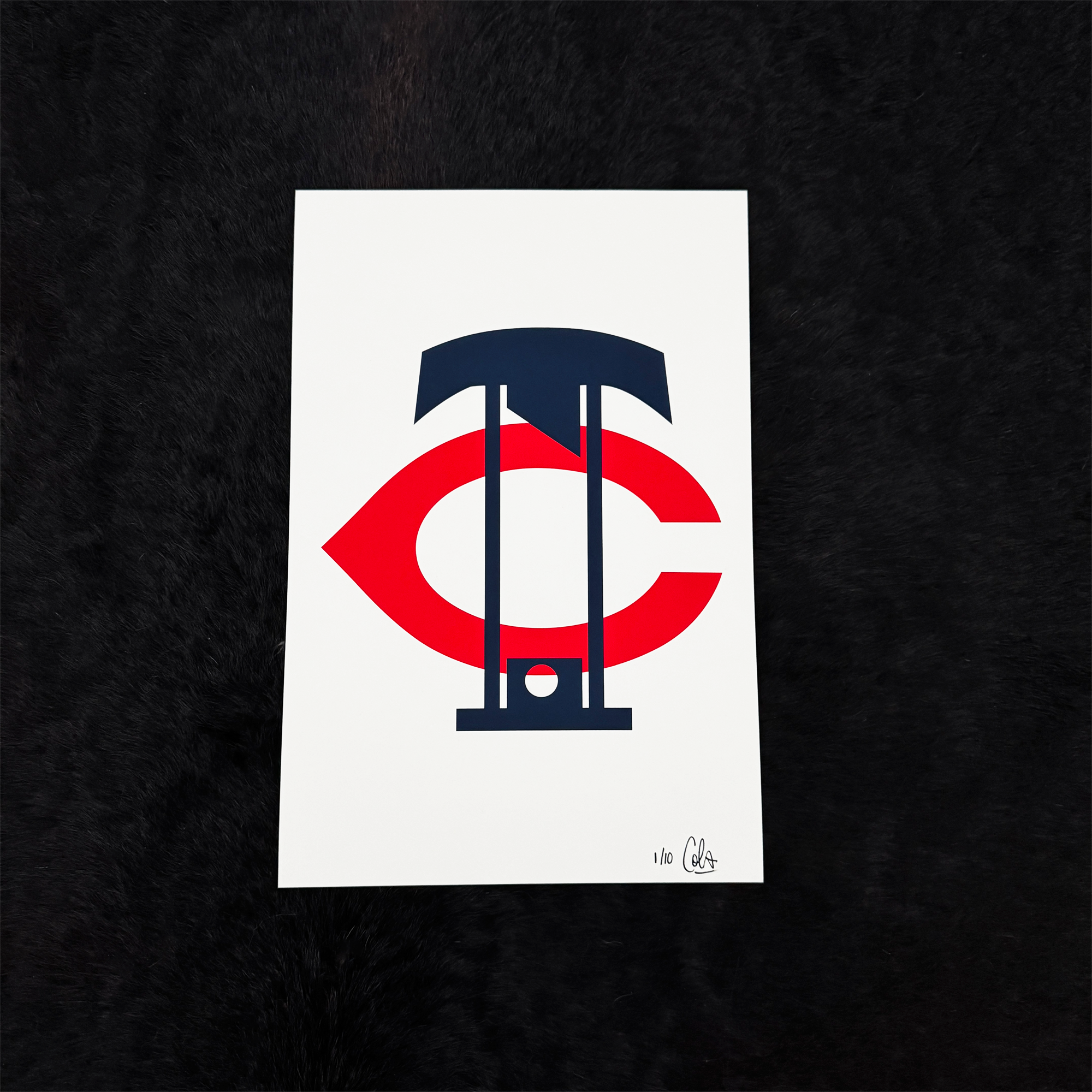 A white print on a black fur background. A navy blue letter T sits above a large red letter C in the style of a sports monogram. Embedded within the letterforms is a navy blue guillotine. Signed and numbered 1/10 in the bottom right corner.