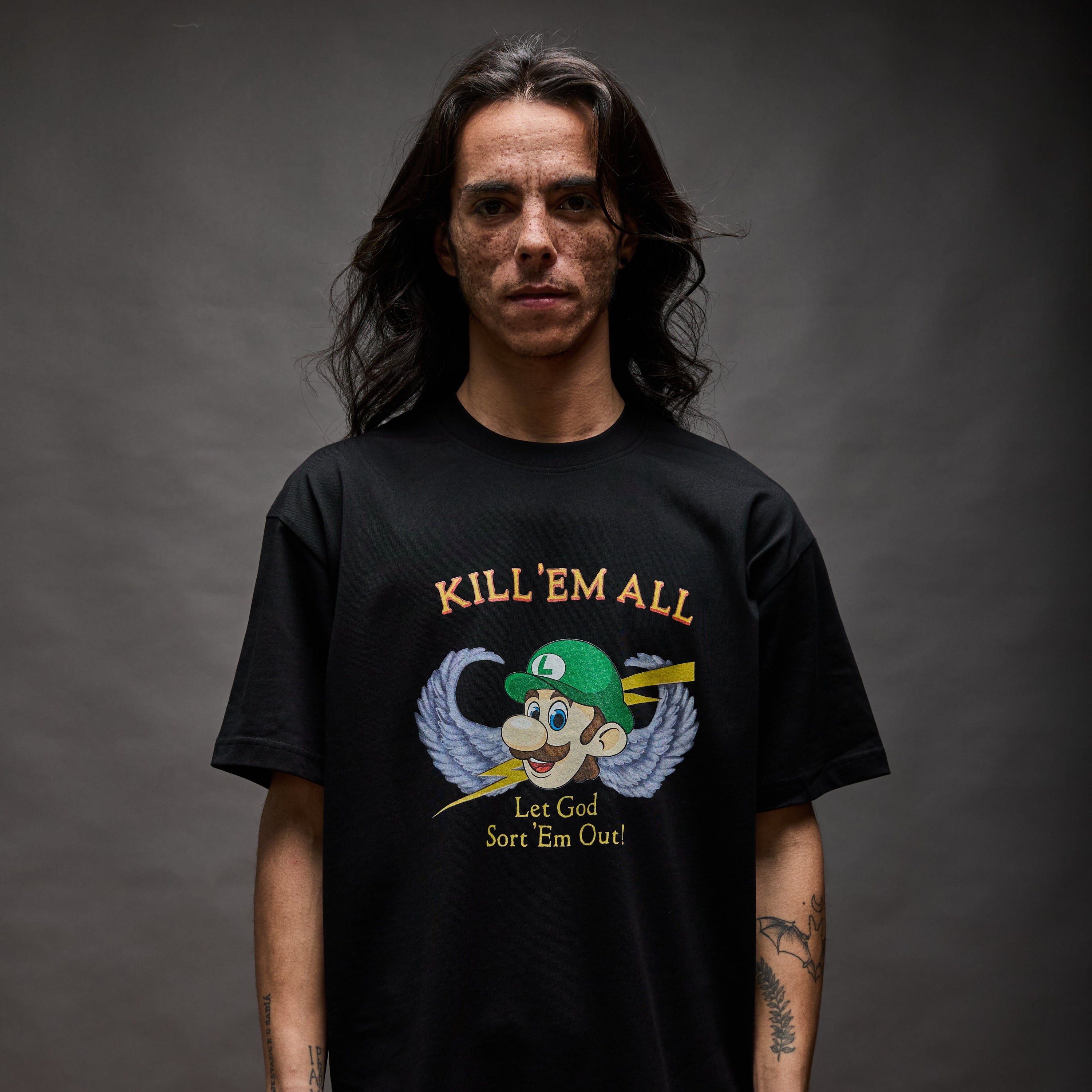 Black T-shirt with “KILL ’EM ALL” in yellow serif text above a winged cartoon character head with lightning bolts; below reads “Let God Sort ’Em Out!”