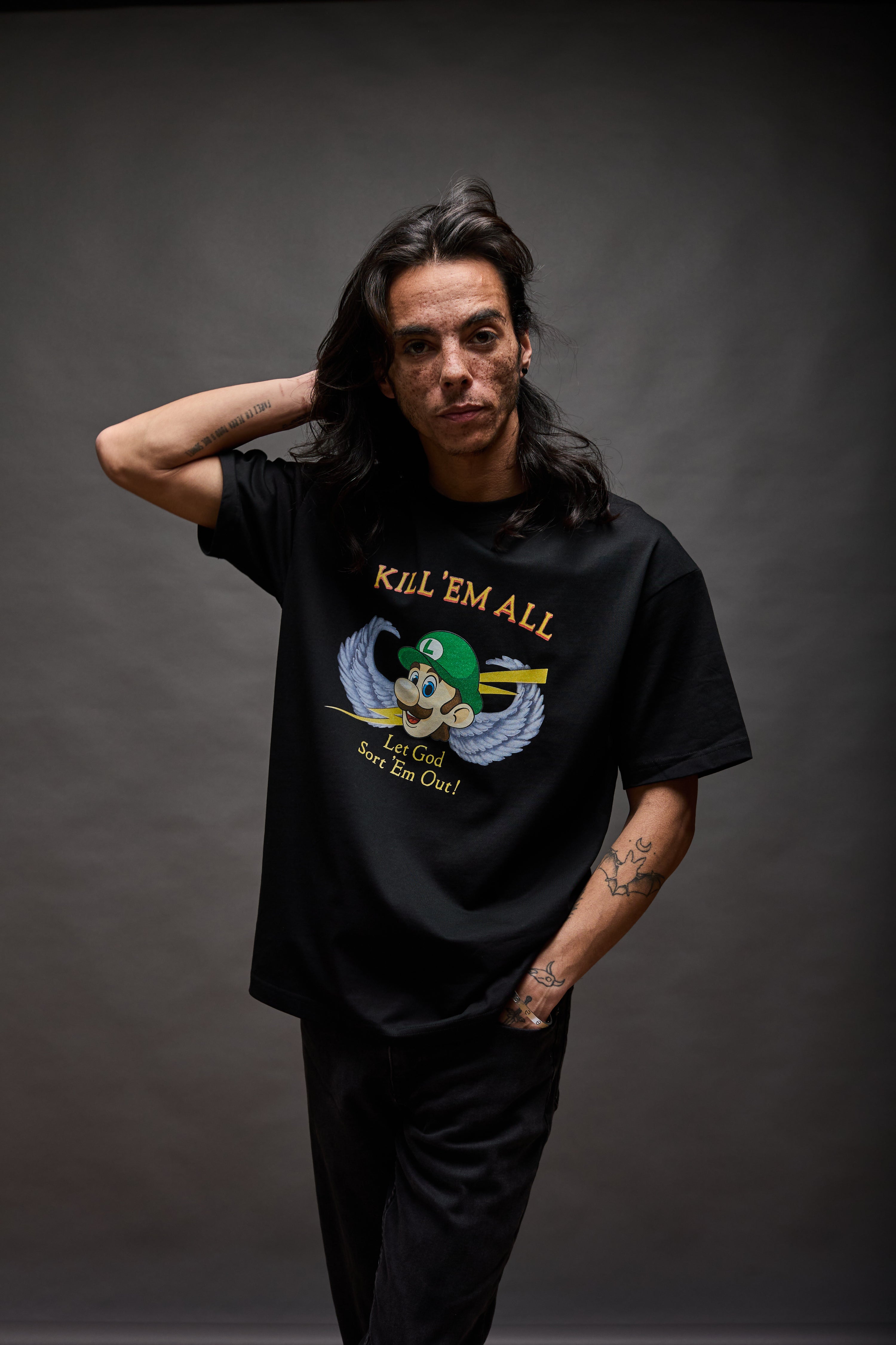 Model wearing black graphic T-shirt with “KILL ’EM ALL” winged character design, standing against a neutral studio background
