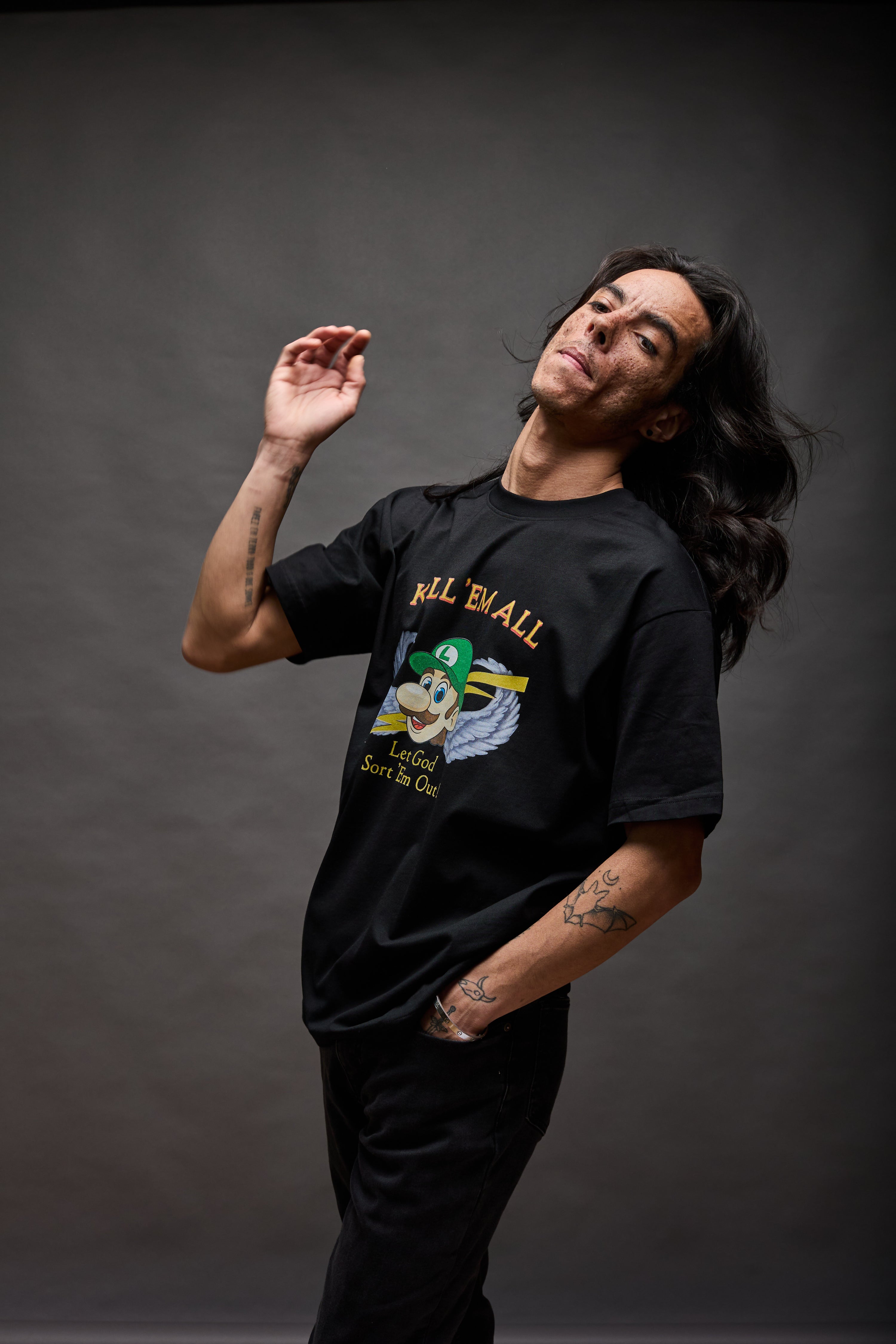 Model wearing black graphic T-shirt with “KILL ’EM ALL” winged character design, standing against a neutral studio background