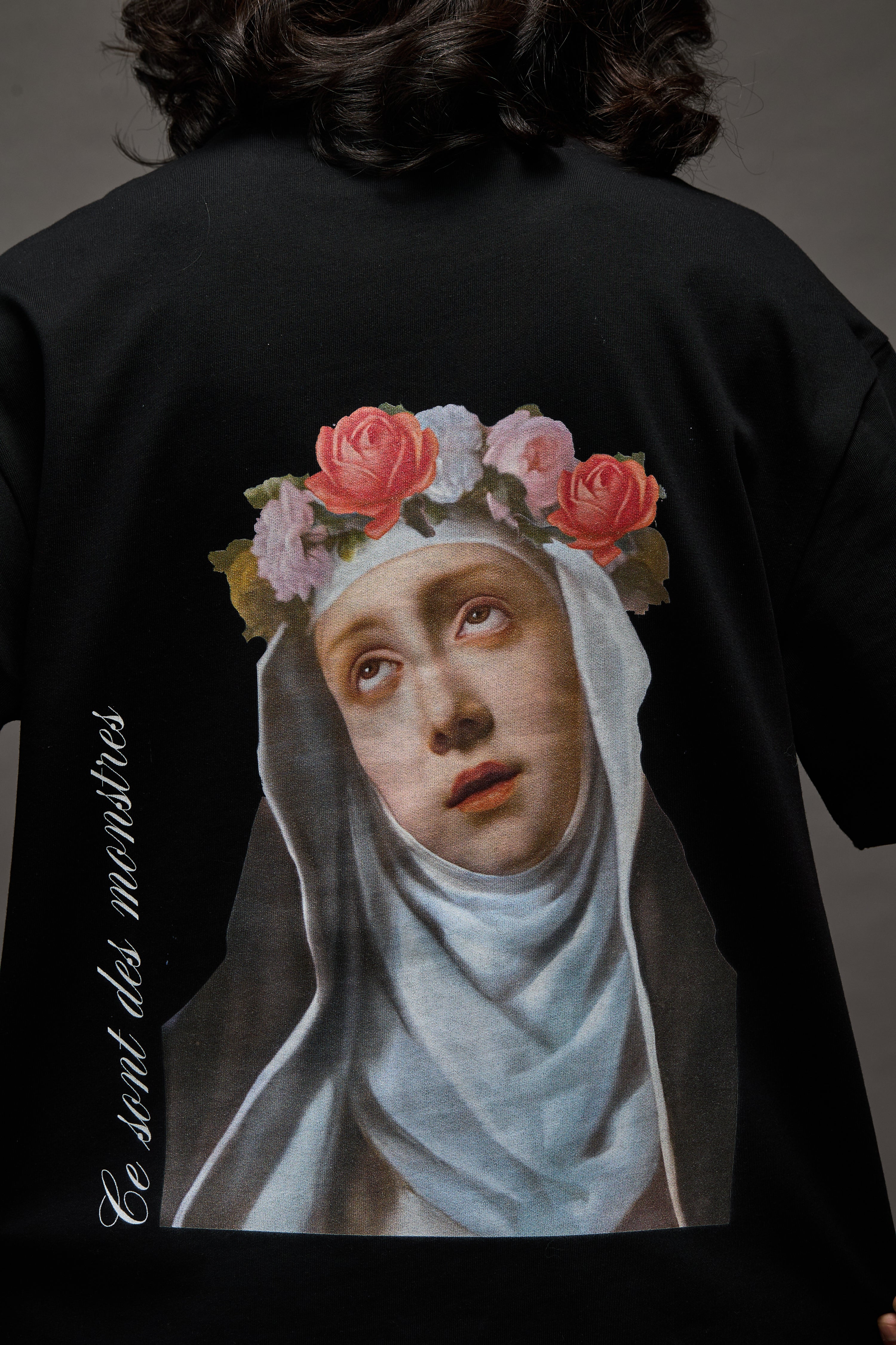 Black t-shirt with a printed design of a Saint Rose de Lima face wearing a nun's headdress and flowers on the back.
